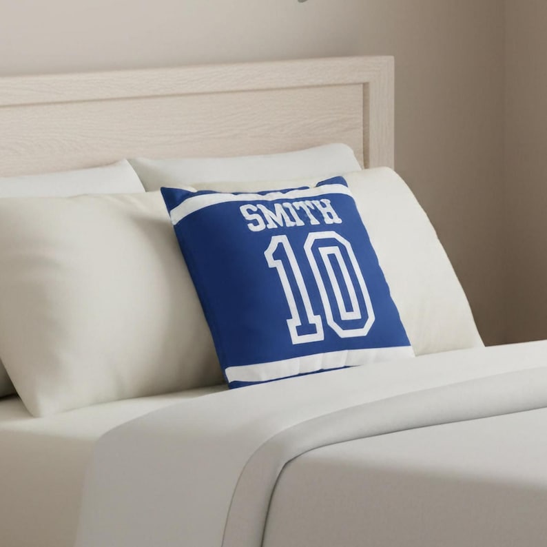 May include: A square throw pillow in royal blue with white horizontal stripes at the top and bottom. The text SMITH is printed in white block letters above the large white number 10, mimicking the appearance of a sports jersey design.