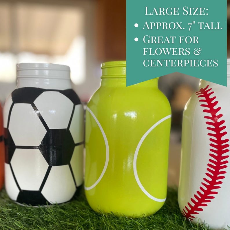 May include: Painted mason jars in a sports theme. The jars are painted to resemble a soccer ball, a tennis ball, and a baseball. The text on the image says "Approx. 7" tall" and "Great for flowers & centerpieces."