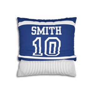 May include: A square throw pillow featuring a blue and white sports jersey design with the name SMITH and the number 10 printed in white block lettering. The bottom section of the pillow displays a contrasting grey and white vertical striped pattern.