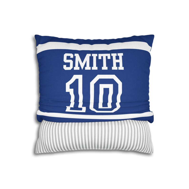 May include: A square throw pillow featuring a blue and white sports jersey design with the name SMITH and the number 10 printed in white block lettering. The bottom section of the pillow displays a contrasting grey and white vertical striped pattern.