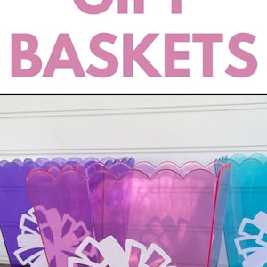 May include: Four clear plastic gift baskets with a cheerleading theme. The baskets are filled with tissue paper and various gifts, including hair ties, hair clips, and other accessories. The baskets are decorated with white cheerleading pom-poms and the names "Ellie", "Chloe", and "Adelyn" are written on the front of the baskets.