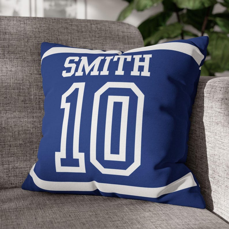 May include: A square throw pillow in royal blue with white accents. The front features the name SMITH in white block lettering above the large white number 10. The design includes white horizontal stripes along the top and bottom edges of the pillow.