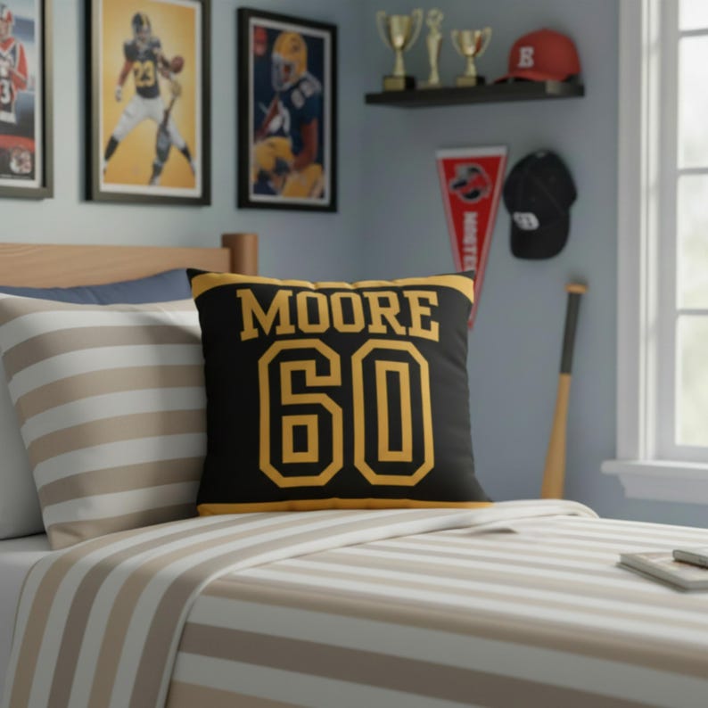 May include: A square decorative throw pillow featuring a black background with yellow text that reads MOORE and the number 60 in a bold athletic font. The pillow has yellow horizontal stripes along the top and bottom edges of the front face.