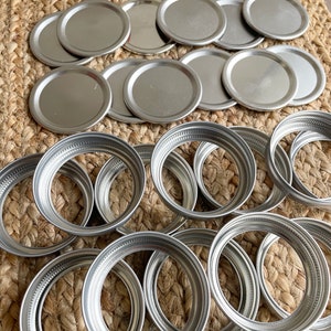 May include: A collection of silver metal jar lids, some are flat and some are ring-shaped.