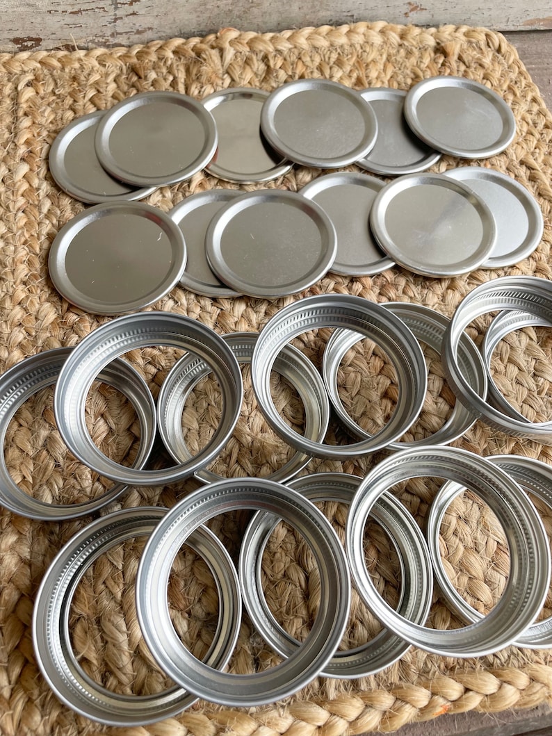 May include: A collection of silver metal jar lids, some are flat and some are ring-shaped.