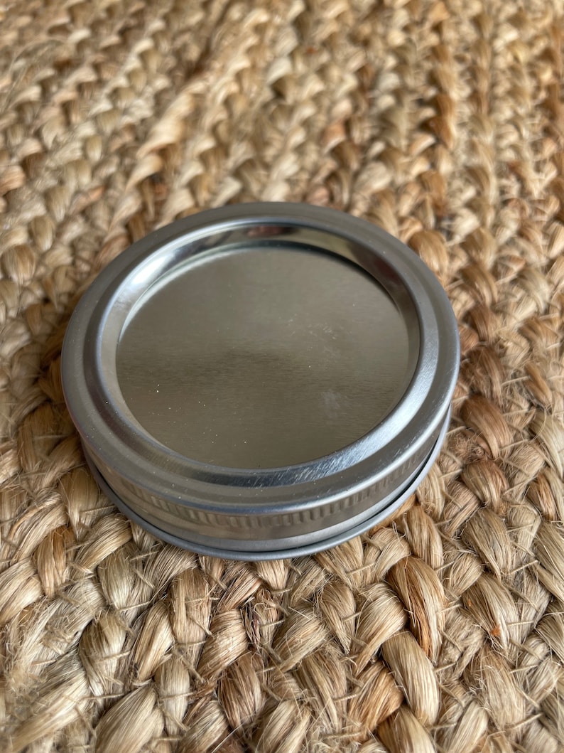May include: A silver metal lid for a jar or container. The lid has a smooth, shiny surface and a slightly raised rim.