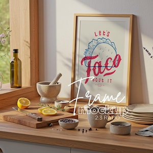 May include: A framed print with the text "Let's Taco Bout It" in red and blue lettering. The print features a stylized illustration of a taco with a red and blue design. The frame is made of wood and has a light brown finish.