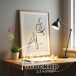 May include: A wooden frame mockup with a black and white line drawing of a person sitting. The frame is on a wooden desk with a black desk lamp and a small green plant in a white pot. The text "Frame Mockup 2:3 Ratio" is written below the frame.