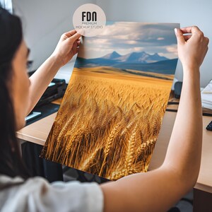 May include: A person holding a photograph of a field of golden wheat with a mountain range in the background.