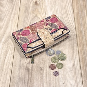 May include: A cork wallet with a zip fastening and a floral pattern in shades of pink, red, and blue. The wallet is open and there are several coins inside.