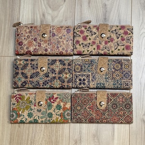Può includere: Sei portafogli in sughero con diversi motivi. I portafogli sono tutti chiusi e hanno una chiusura a zip. I motivi includono disegni floreali, geometrici e astratti. I portafogli sono tutti realizzati in sughero e hanno un colore marrone naturale.
