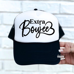 May include: A white and black trucker hat with the text "Extra Boujee" in black script font.