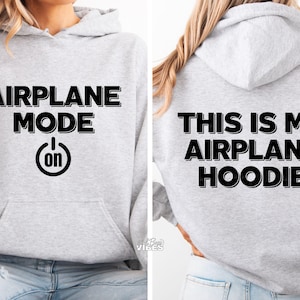 Puede incluir: Una sudadera con capucha gris claro con las palabras "AIRPLANE MODE" encima de un s&iacute;mbolo de bot&oacute;n de encendido con "on" dentro. La parte trasera de la sudadera con capucha dice "THIS IS MY AIRPLANE HOODIE" en letras negras. La sudadera tiene un bolsillo delantero y una capucha.