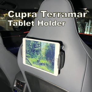 May include: A black tablet holder mounted on the back of a car seat. The holder is holding a white tablet displaying a nature scene. The text "Cupra Terramar Tablet Holder" is at the top of the image.