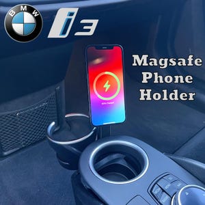 以下が含まれることがあります： 充電中のiPhoneを備えた黒いMagSafeフォンホルダー。電話は充電シンボルを表示します。ホルダーは車のカップホルダーに取り付けられています。「Magsafe Phone Holder」のテキストが表示されます。