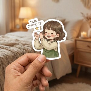 Op de afbeelding: Een sticker met een cartoon illustratie van een lachende persoon die klapt. De persoon heeft bruin haar en draagt een groene overall jurk en een beige trui. De tekst op de sticker luidt "TASK COMPLETE!" met een ster.