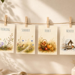 Puede incluir: Cuatro tarjetas rectangulares colgadas de un cordel con pinzas de madera. Cada tarjeta presenta una ilustración estacional en acuarela y texto: FRÜHLING con azafranes, SOMMER con un pájaro, HERBST con una calabaza y manzanas, y WINTER con una pajarera.