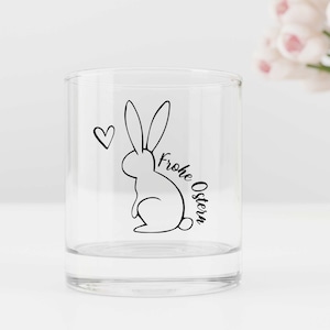 Könnte beinhalten: Ein klares Glas mit einer schwarz-weißen Illustration eines Hasen und dem Text "Frohe Ostern" an der Seite.
