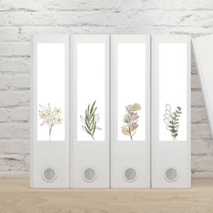 Może przedstawiać: Pięć białych teczek z różnymi rysunkami roślin na froncie. Rośliny są narysowane czarnymi i brązowymi liniami. Teczki są ułożone w rzędzie na jasnobrązowej powierzchni.