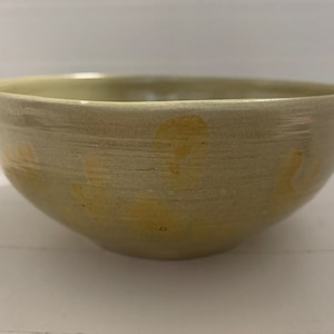 May include: A light beige ceramic bowl with a slightly textured surface and subtle brown speckles throughout. The bowl has a rounded shape and a slightly flared rim.