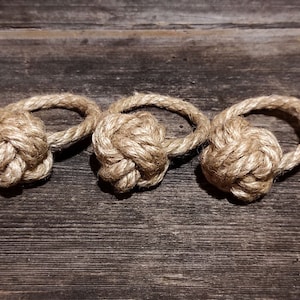 May include: Three brown rope napkin rings tied in a knot. The rings are on a rustic wooden surface.