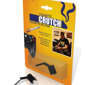 May include: A black plastic cigarette holder called "Cigarette Crutch" that attaches to a gaming controller. The holder is shown attached to a black Xbox controller. The packaging is yellow with black text and a picture of a person holding a cigarette and a controller.
