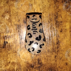 May include: A gold glitter and black leopard print phone grip with the word "Mama" written in black cursive.