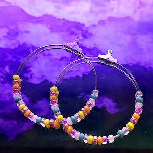May include: A pair of silver hoop earrings with colorful beads. The beads are in shades of yellow, orange, pink, teal, and white.