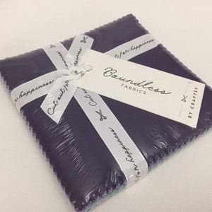 May include: A square bundle of dark purple fabric squares, wrapped in clear plastic and tied with a white ribbon. The ribbon has the text "Cut out for happiness" printed on it. A white tag reads "Boundless Fabrics" and "By Craftsy".