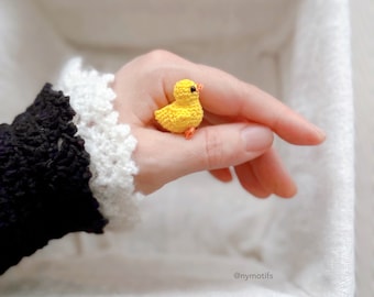 May include: A small crocheted yellow chick with orange feet and black eyes. The chick is being held in a hand.