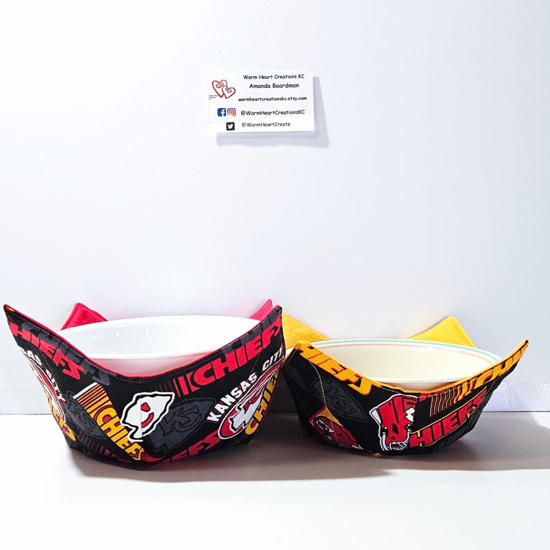 May include: Two fabric bowl cozies in black, red, and yellow with the Kansas City Chiefs logo and text. The larger cozy is red and the smaller cozy is yellow.
