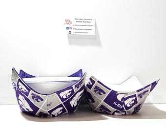 May include: Two purple and gray fabric bowl cozies with the Kansas State University Wildcats logo. The cozies are folded and ready to use.