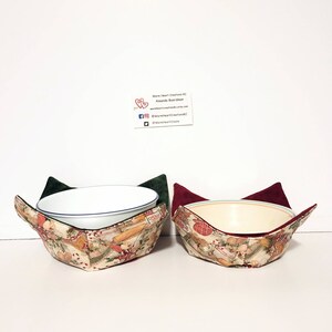 May include: Two fabric bowl cozies with a Christmas-themed print. The cozies are folded and have a green and red velvet lining. The cozies are designed to keep bowls warm.