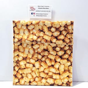 May include: A square, fabric pouch with a repeating pattern of golden-brown tater tots. The pouch has a flap closure. A small white card with text is in the upper left corner. The text on the card reads "Warm Heart Creations" and social media handles.