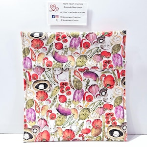 May include: A white fabric bag with a colorful vegetable pattern, including tomatoes, eggplants, artichokes, and mushrooms. The bag has a flap closure. A small white card with text is in the upper left corner.