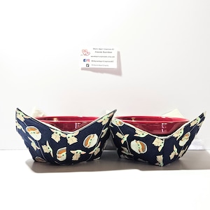 May include: Two red bowls with navy blue and green fabric bowl cozies featuring a repeating pattern of a cartoon character from the Star Wars franchise. The cozies are lined with white fabric.