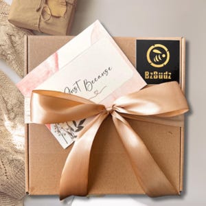 May include: A brown cardboard box tied with a gold ribbon and a card that says "Just Because". The box has a black sticker with a bee logo and the text "BzBuddz".