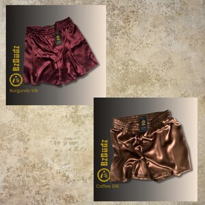 May include: Two pairs of satin shorts in burgundy and coffee colors. The shorts have an elastic waistband and a relaxed fit. The brand name "BzBuddz" is printed on the shorts.