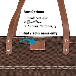 K&ouml;nnte beinhalten: Braune Canvas-Tragetasche mit Ledergriffen und einem braunen Leder-Patch zur Personalisierung. Der Text "Font Options" ist &uuml;ber dem Text "1. Book Antique", "2. Great Vibes" und "3. Lucida Calligraphy" gedruckt. Der Text "Initial / Your name only" ist unter dem Patch gedruckt.