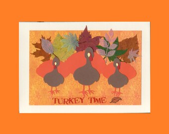 May include: A rectangular greeting card featuring three brown turkey cutouts with red wattles and orange feet. Behind the turkeys are orange cloud shapes and various autumn leaves in shades of green, brown, and purple. The text TURKEY TIME is printed.