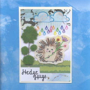 May include: A greeting card with a hedgehog holding flowers, a green tree, and clouds with raindrops in various colors. The text "Hedge Hugs" is written on the card.