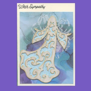 May include: A sympathy card with the words "With Sympathy" printed on the front. The card features a cutout of an angel with a blue and gold design.
