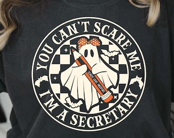 May include: A black t-shirt with a white circle graphic featuring a ghost holding a pencil with the text "You Can't Scare Me I'm A Secretary" in a black and white checkered pattern.