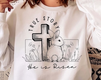 May include: White sweatshirt with a black and white graphic of a cross and a rabbit. The text "True Story" is above the graphic and the text "He is Risen" is below the graphic.