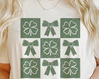 Puede incluir: Camiseta color crema con un patrón de cuadrícula verde de tréboles y lazos. El diseño tiene un aspecto envejecido y vintage. Esta camiseta informal es adecuada para el uso diario, ideal para el Día de San Patricio o cualquier ocasión.