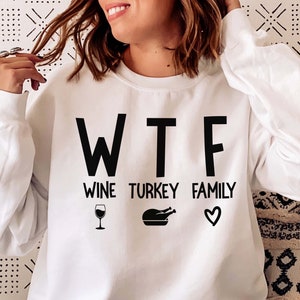 May include: White sweatshirt with the text "WTF Wine Turkey Family" in black lettering. The text is accompanied by a wine glass, a turkey, and a heart.
