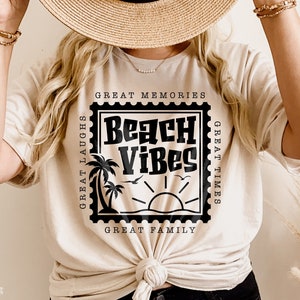 Puede incluir: Una camiseta blanca con un gr&aacute;fico negro de un sello con el texto "Beach Vibes" en su interior. El sello tiene el texto "Great Memories", "Great Times", "Great Laughs" y "Great Family" alrededor.
