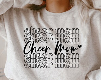May include: A gray sweatshirt with the text "Cheer Mom" repeated multiple times in a retro font. The text is in black and the sweatshirt has a relaxed fit.