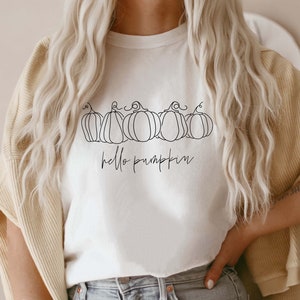 May include: White t-shirt with a line drawing of five pumpkins and the text "hello pumpkin" in black.