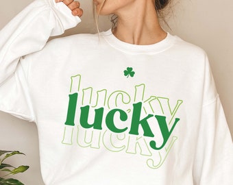 May include: White sweatshirt with a green "lucky" graphic in a layered font style. A small green shamrock is above the word.